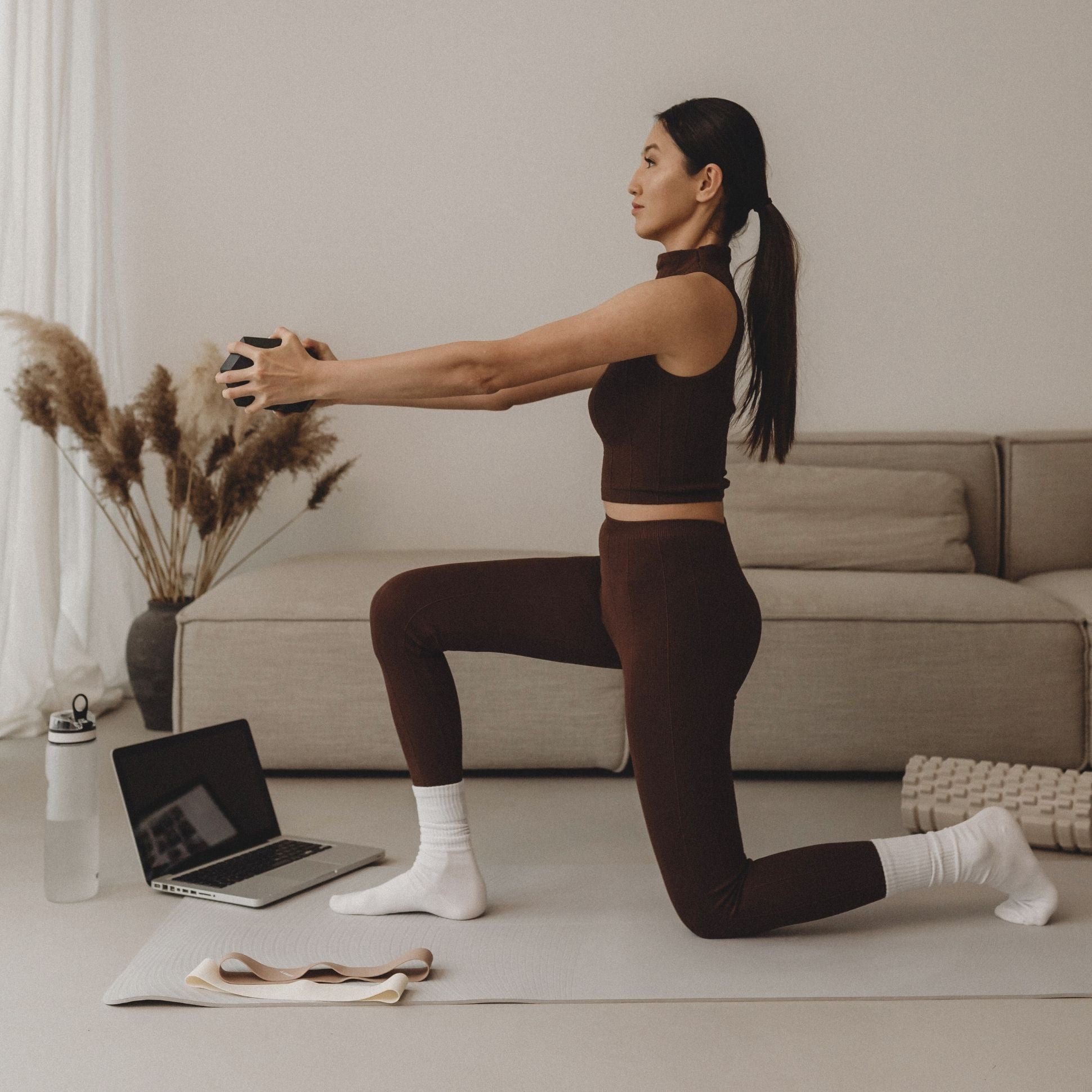 Woman exercising on a mat in a living room with a laptop.