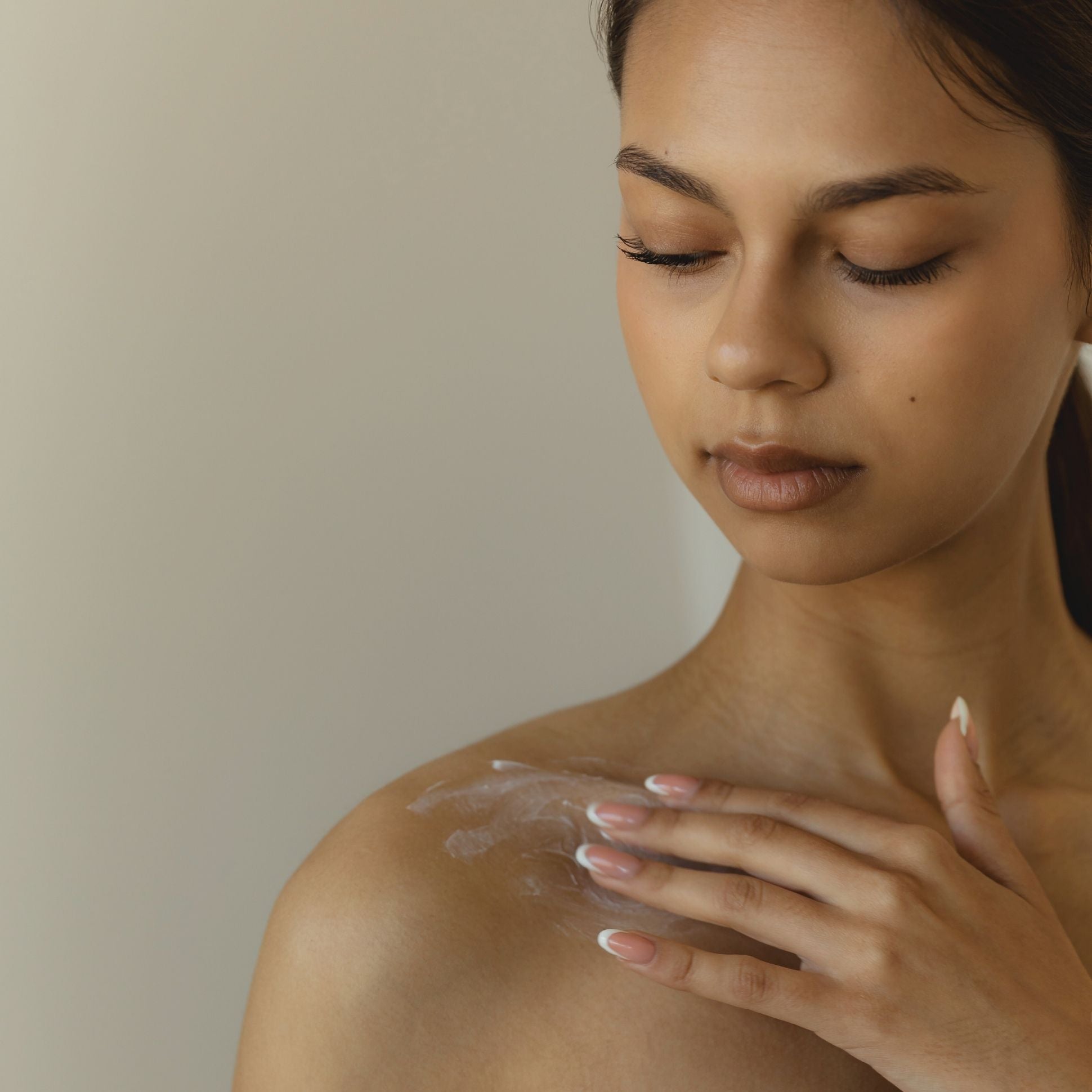 Woman applying a skincare product to her shoulder against a neutral background