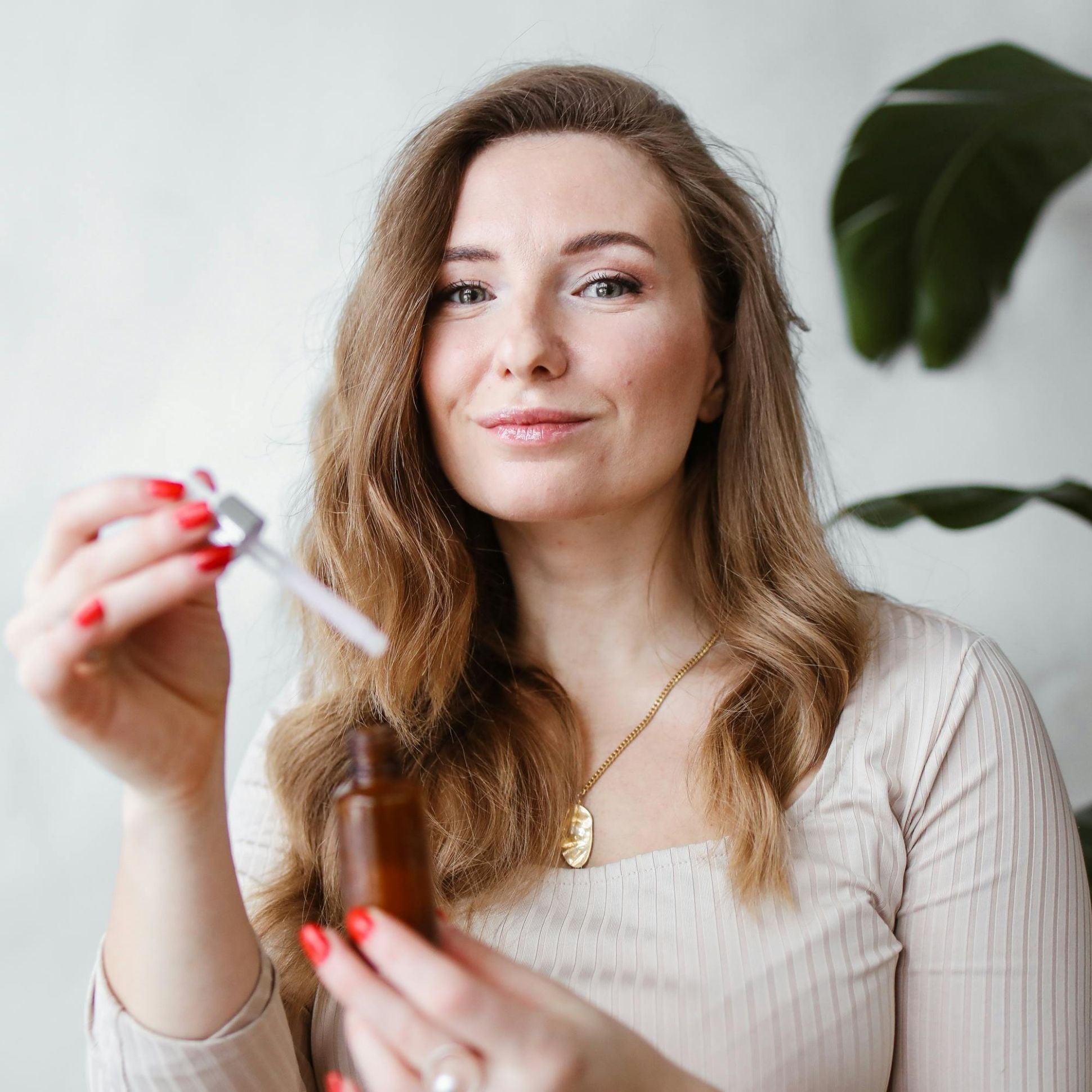 Woman holding a brown bottle and a dropper with a plant in the background